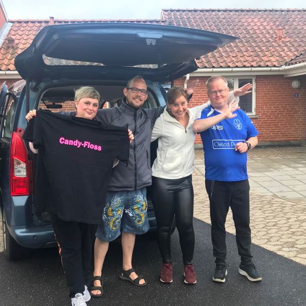 Fire personer smiler og er glade. En af personerne holder en t-shirt med teksten "Candy-Floss".