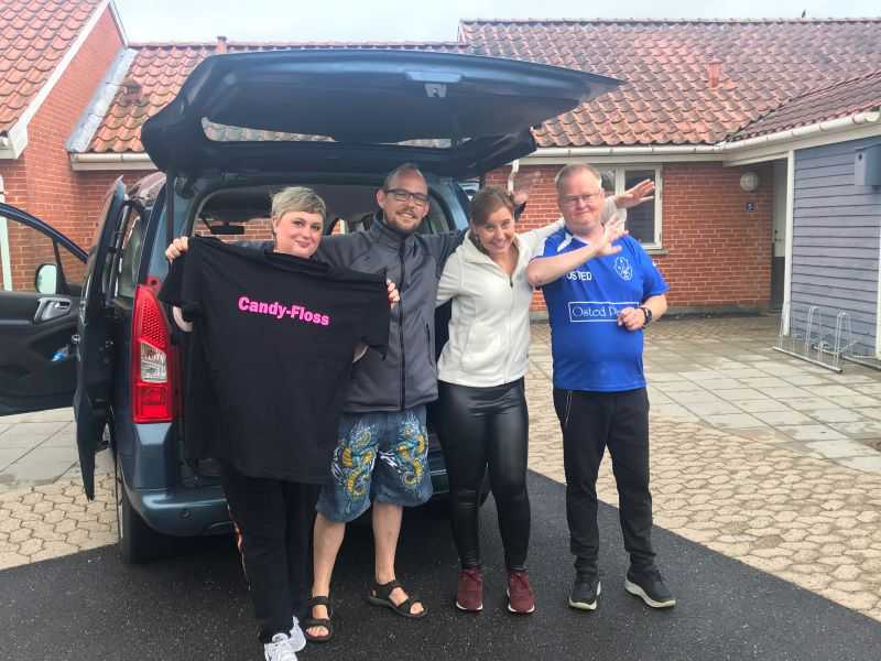 Fire personer smiler og er glade. En af personerne holder en t-shirt med teksten "Candy-Floss".