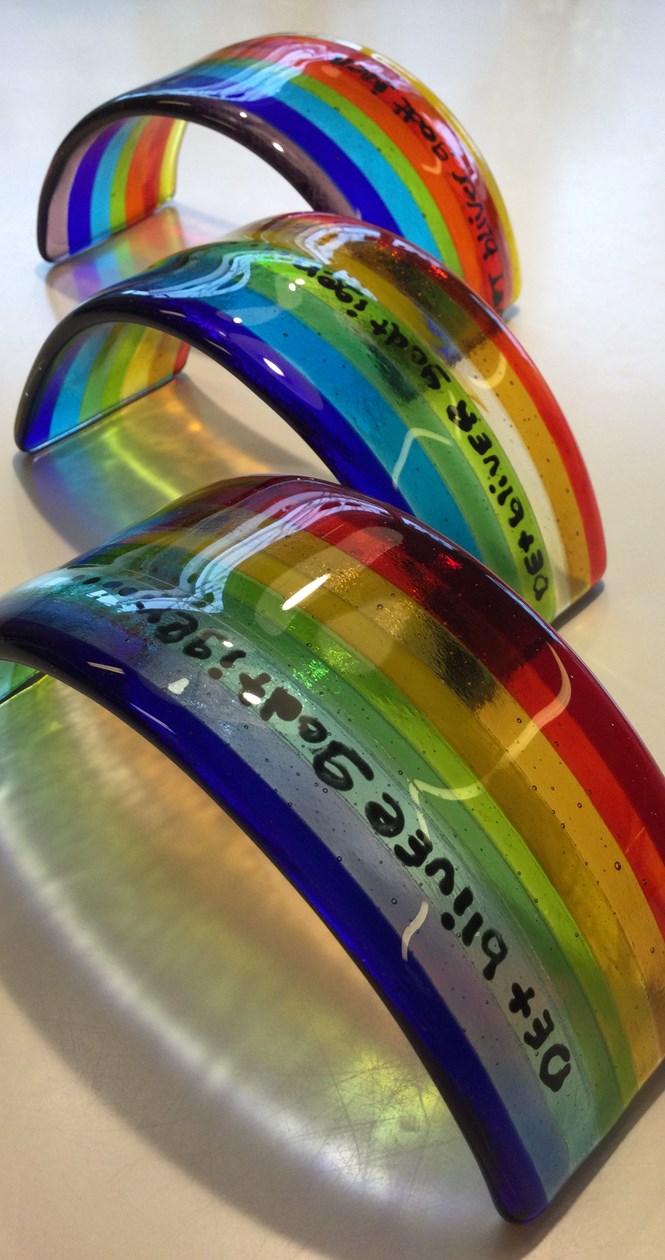 Fint kunst lavet af glas. Det forestiller tre regnbuer med tekst.