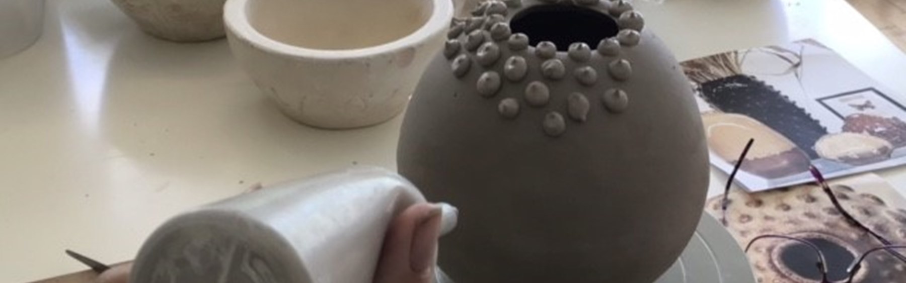 Keramikkrukke, der ikke er færdig endnu. En person er ved at lave små prikker med ler på krukken.