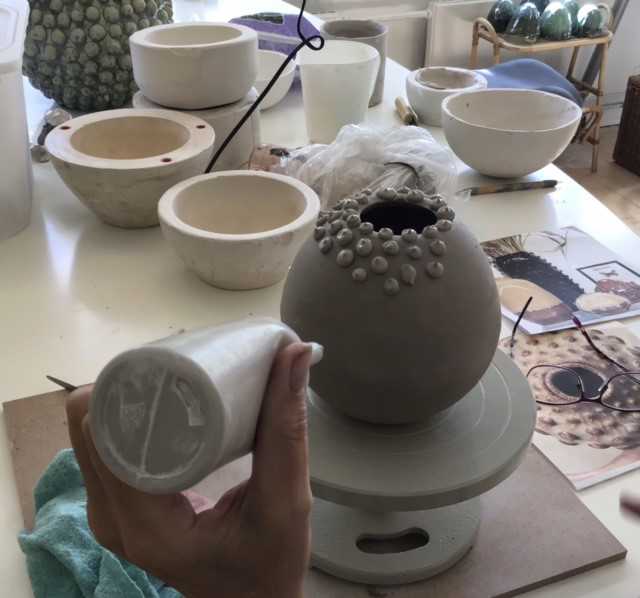 Keramikkrukke, der ikke er færdig endnu. En person er ved at lave små prikker med ler på krukken.