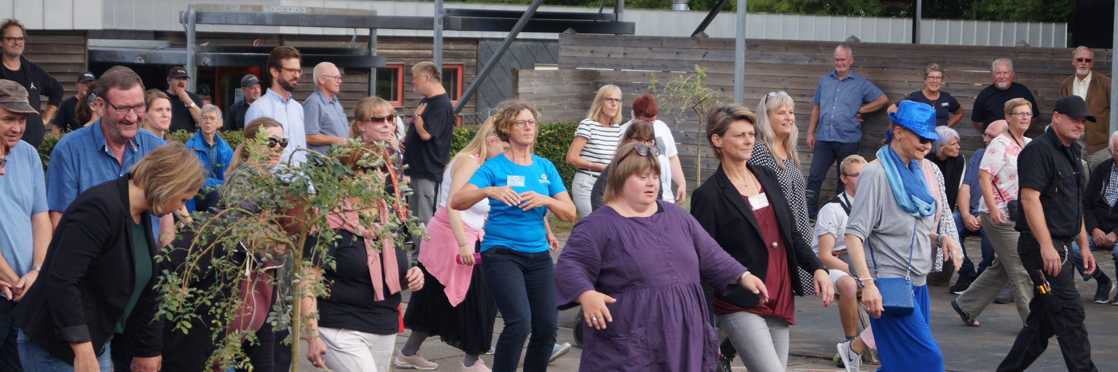 En masse mennesker, der danser en fælles dans. De smiler og er glade.