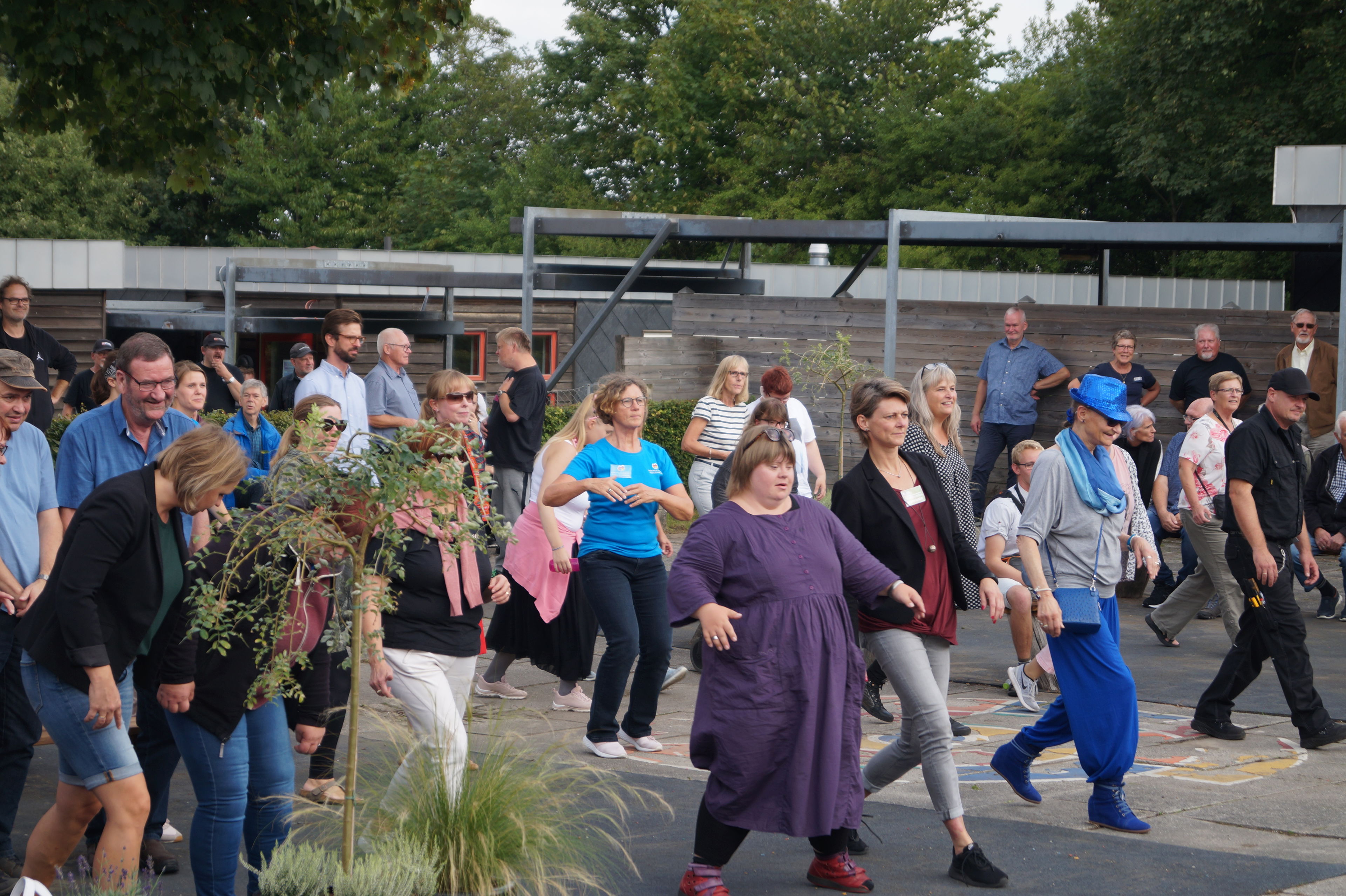 En masse mennesker, der danser en fælles dans. De smiler og er glade.