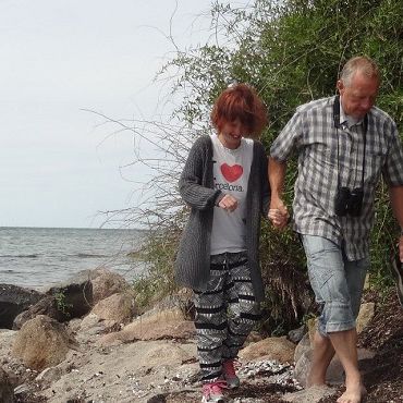 To personer går på en strand og holder i hånd. Man kan se vandet i baggrunden.