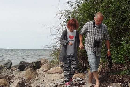 To personer går på en strand og holder i hånd. Man kan se vandet i baggrunden.