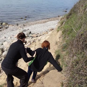 To personer går på en strand. De er på vej ned ad en lille skrænt. Den ene holder ved den anden, så de ikke falder.