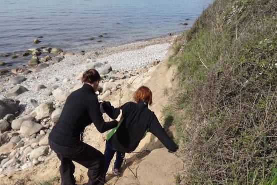 To personer går på en strand. De er på vej ned ad en lille skrænt. Den ene holder ved den anden, så de ikke falder.