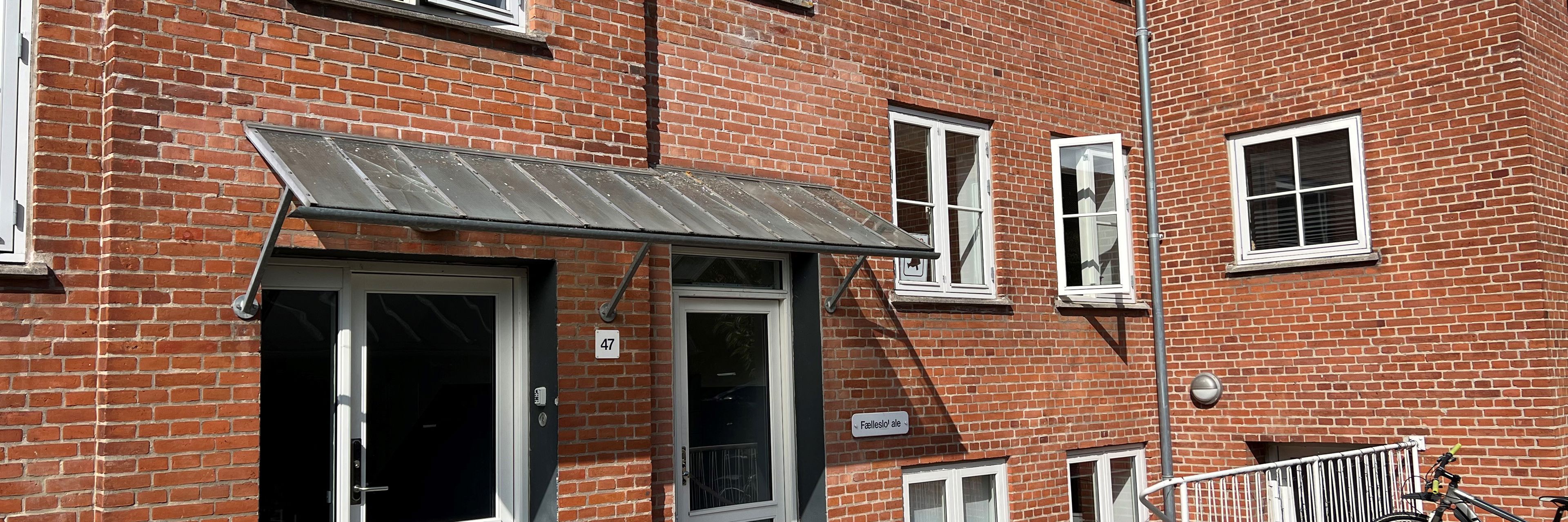 En rød murstensbygning med åbne vinduer. En kvinde kigger ud af vinduet og vinker.