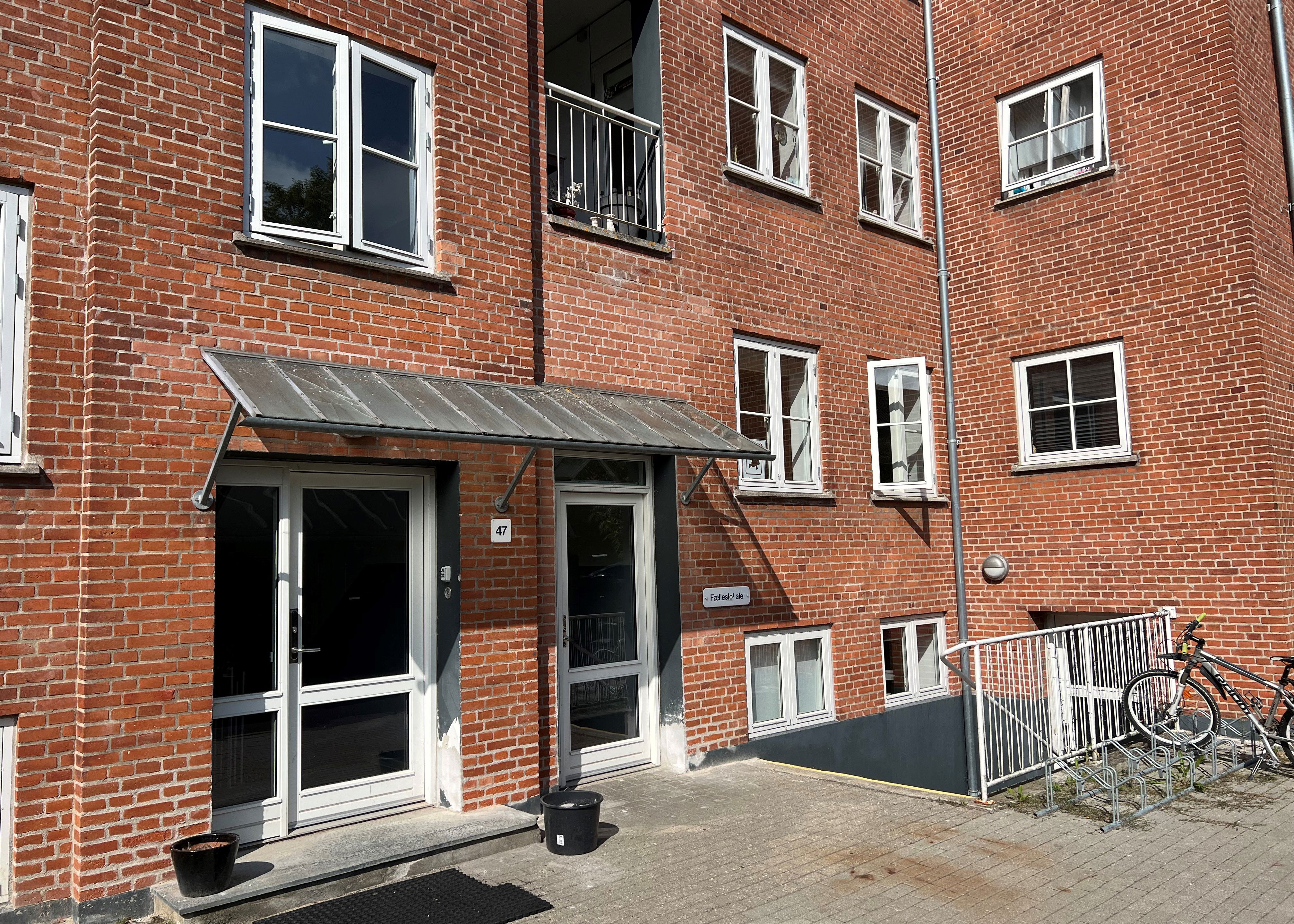 En rød murstensbygning med åbne vinduer. En kvinde kigger ud af vinduet og vinker.