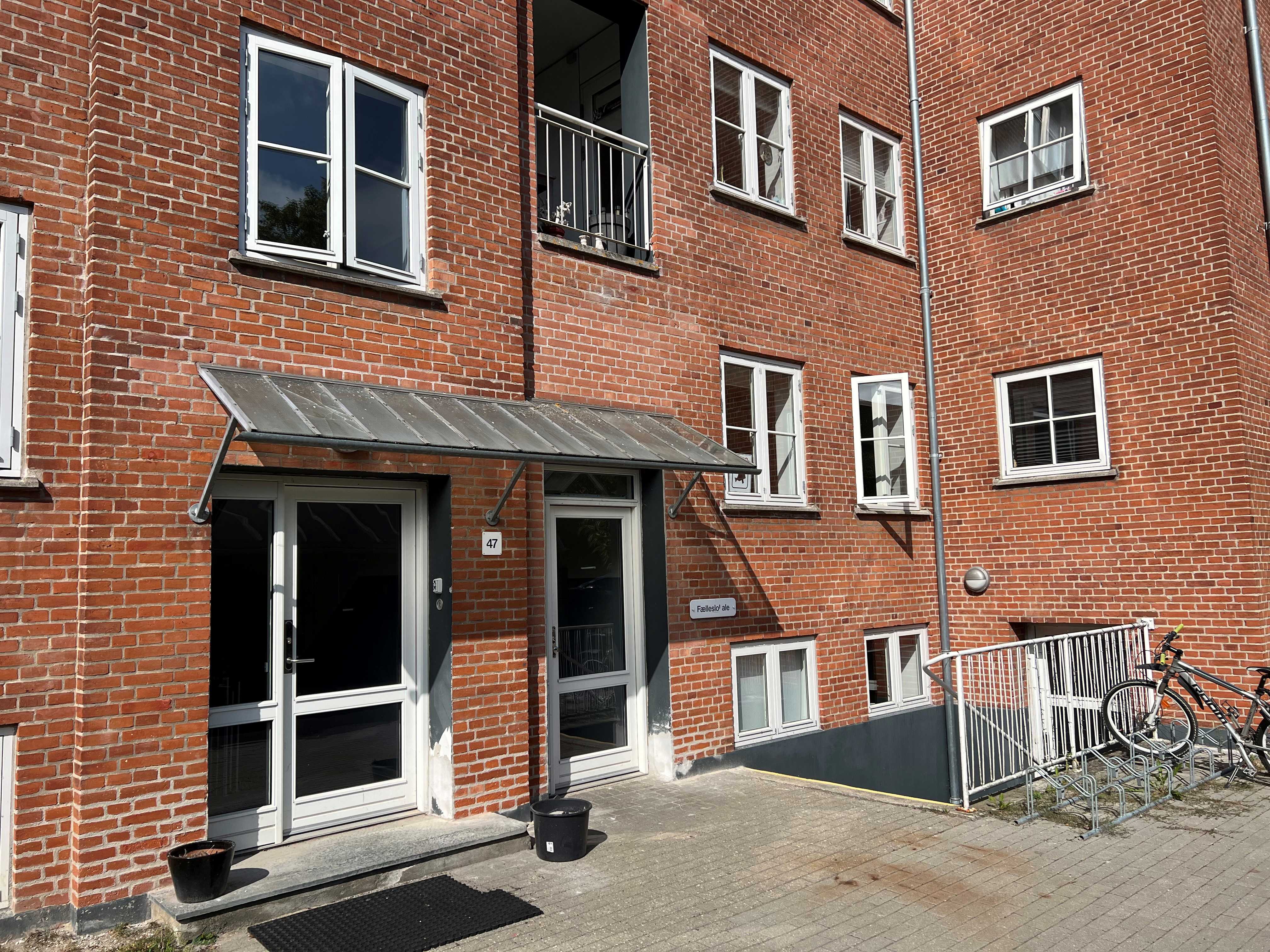 En rød murstensbygning med åbne vinduer. En kvinde kigger ud af vinduet og vinker.