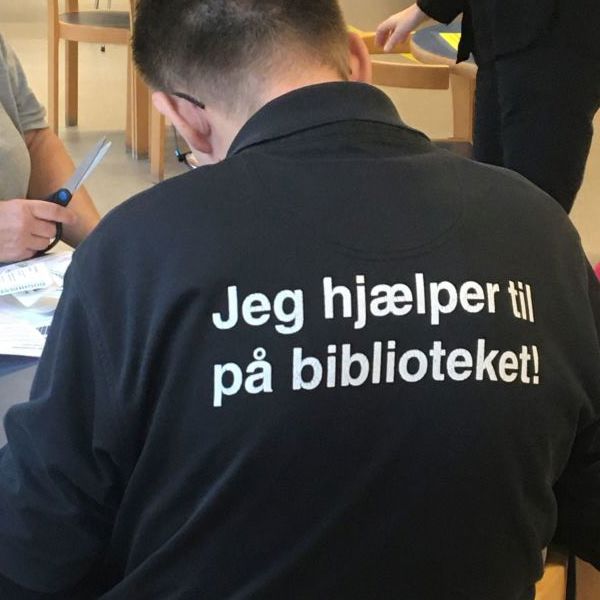 Person sidder med ryggen til. Han har en trøje på, hvor der står, at han hjælper til.