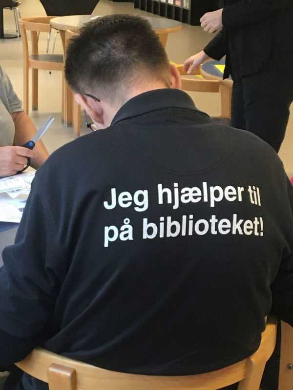 Person sidder med ryggen til. Han har en trøje på, hvor der står, at han hjælper til.