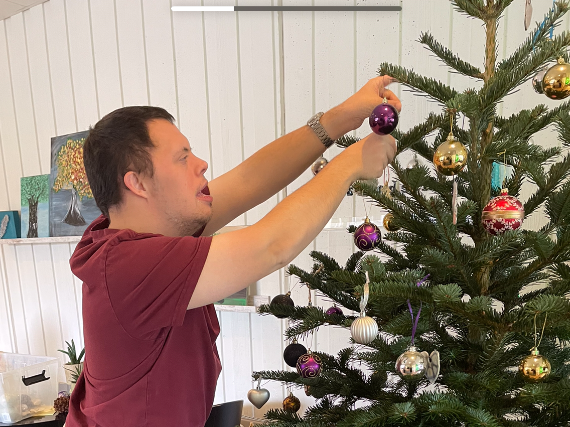 Mand hænger julekugler på et juletræ.