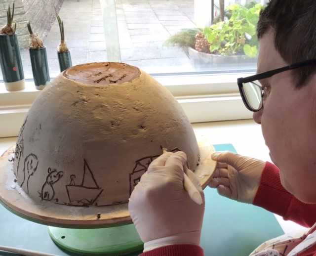 Person laver en skål i keramik. Der er tegninger på, heriblandt af en båd.