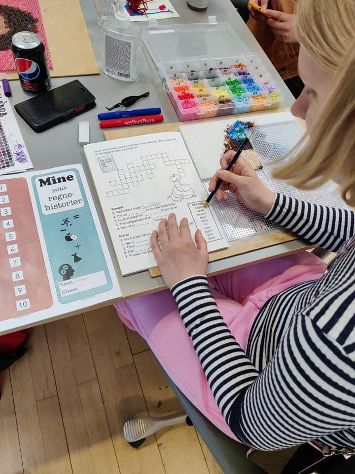 Person laver et krydsord. Der er tuscher og perler på bordet.