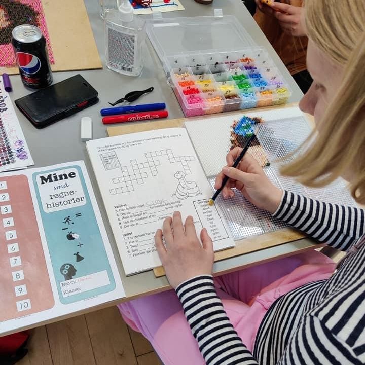 Person laver et krydsord. Der er tuscher og perler på bordet.